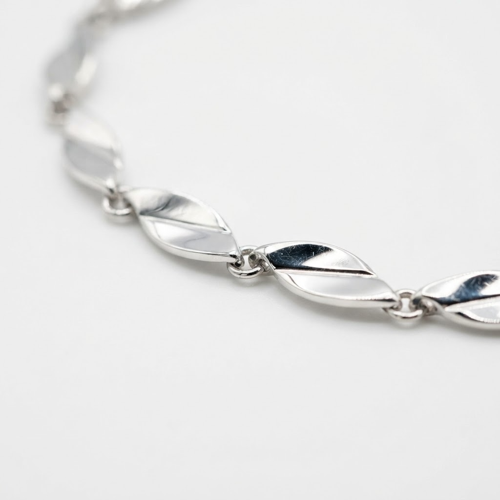 Silver-toned wave link bracelet detail – flat twisted leaf-shaped mirror links with polished faceted surfaces creating fluid wave pattern – extreme close-up product photography