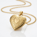 Goudkleurig hartvormig medaillon met ornamentele gravure op reflecterend wit oppervlak, toont glanzende afwerking en spiegeling aan gouden ketting