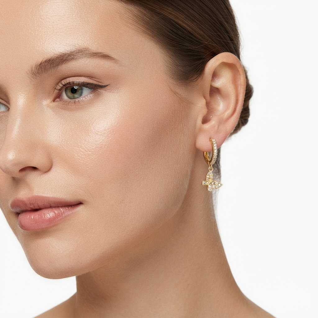 Woman wearing gold-toned huggie hoop earrings with pavé crystals and butterfly charm - elegant crystal huggie earrings styling photo - luxury jewelry lifestyle photography