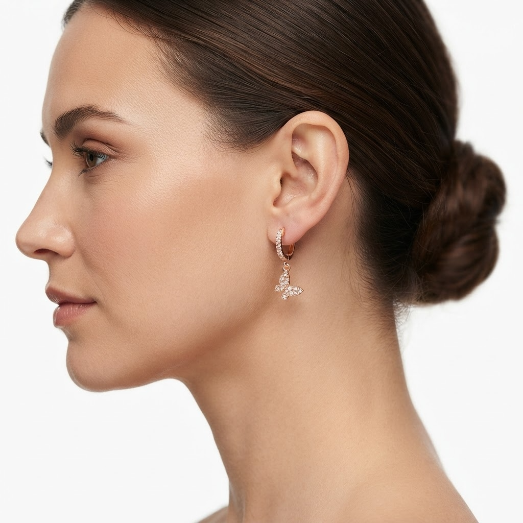 Woman wearing rose gold-toned huggie hoop earrings with pavé crystals and butterfly charm - elegant crystal huggie earrings styling photo - luxury jewelry lifestyle photography