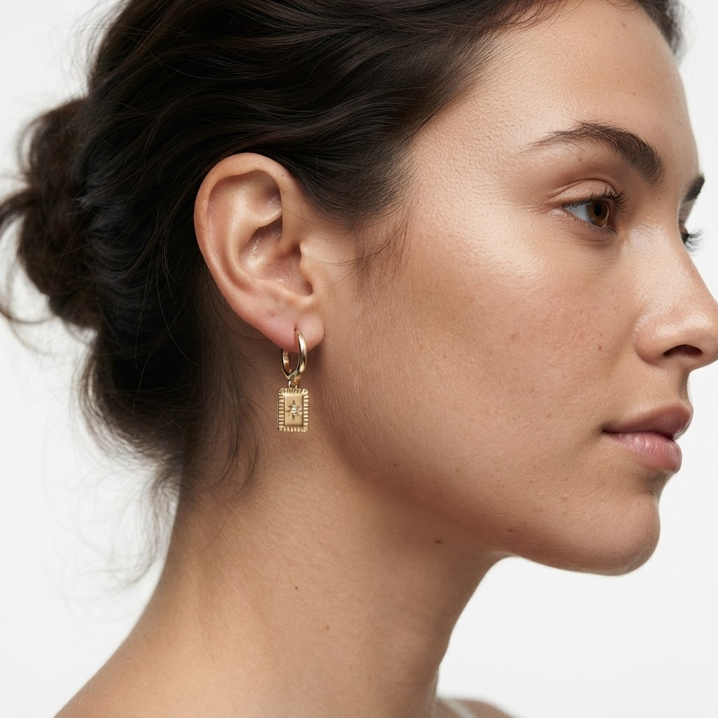 Woman wearing gold-toned huggie hoop earrings with star medallion pendant - elegant textured rectangular charm earrings styling photo - luxury jewelry lifestyle photography