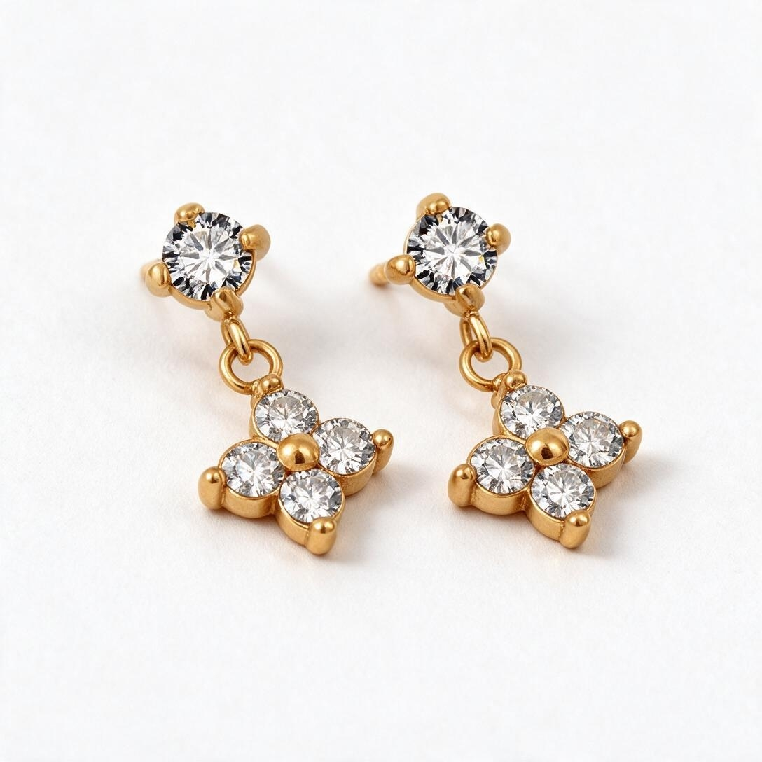 Gold-tone stud earrings with four-petal flower dangle set with small clear crystals around a center bead, studio pair on white